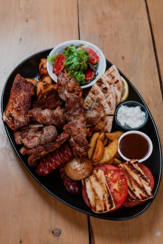 Mouthwatering Mediterranean platter with grilled meats, vegetables, and dips on a wooden table.