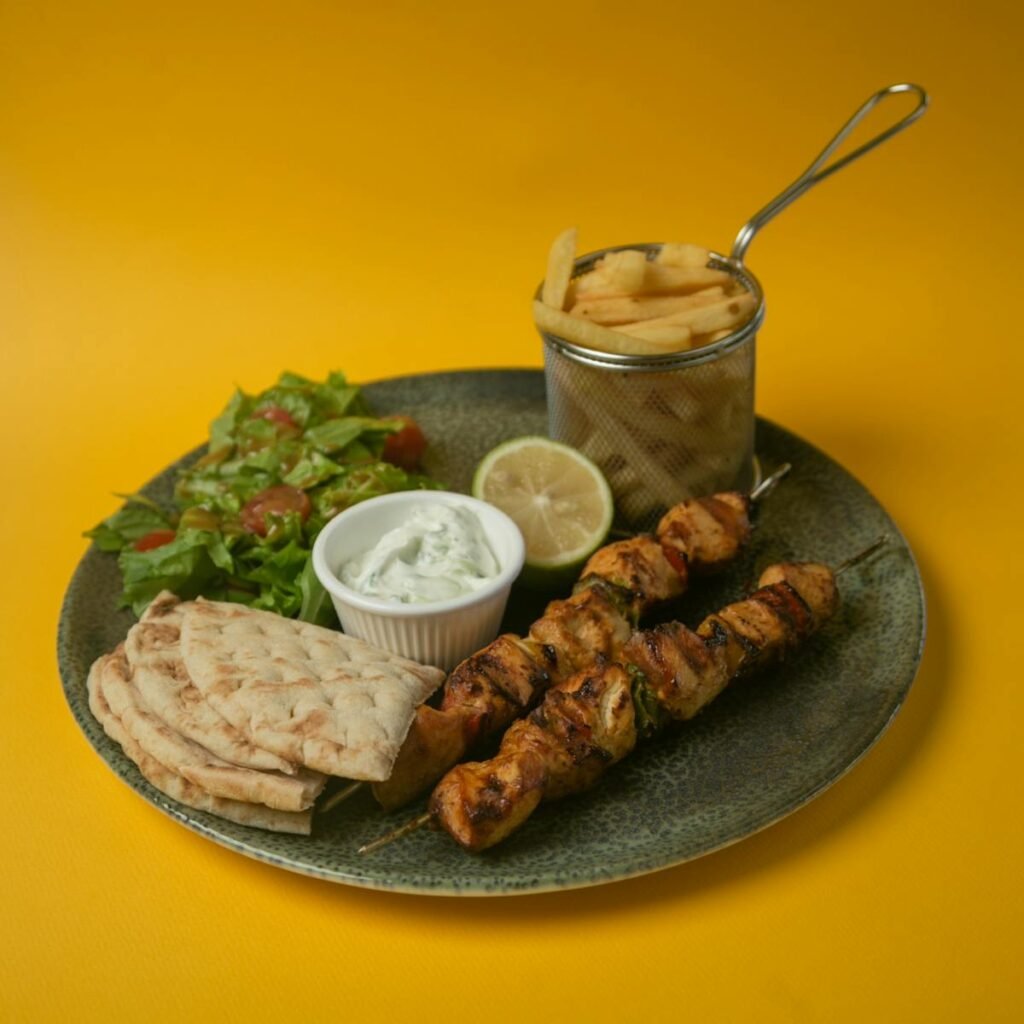 A beautifully presented Greek meal featuring souvlaki, fries, tzatziki, pita, salad, and lemon slice.