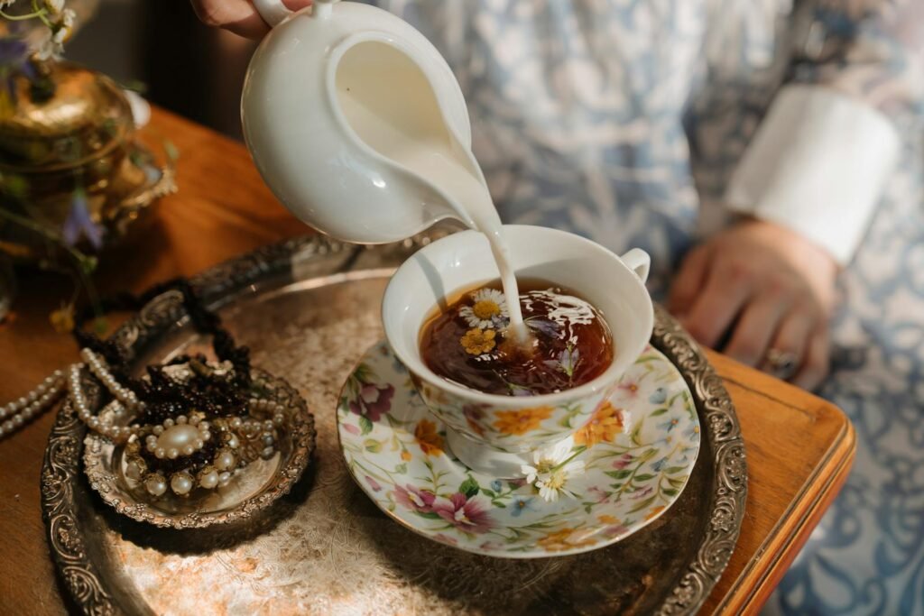 A vintage tea scene with milk being poured into chamomile tea, surrounded by pearls and ornate jewelry.