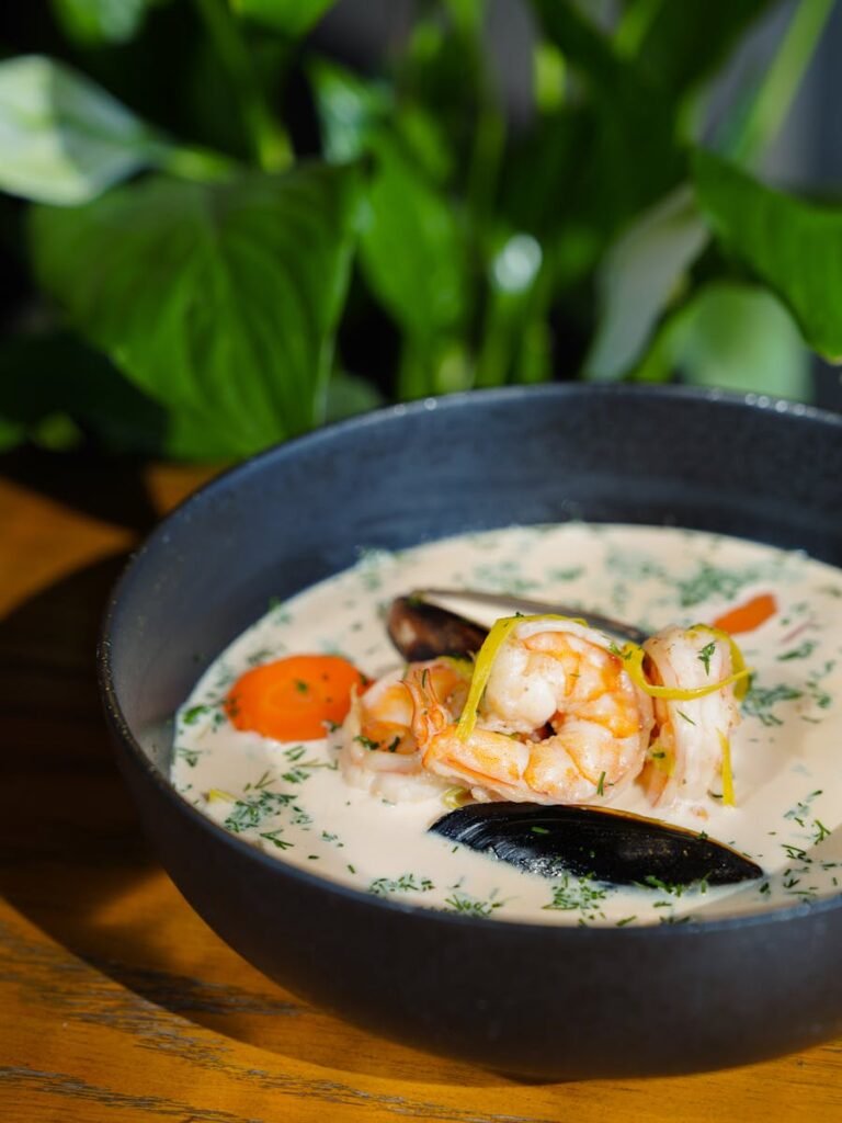Close-up of creamy seafood chowder with shrimp and mussels in a black bowl.