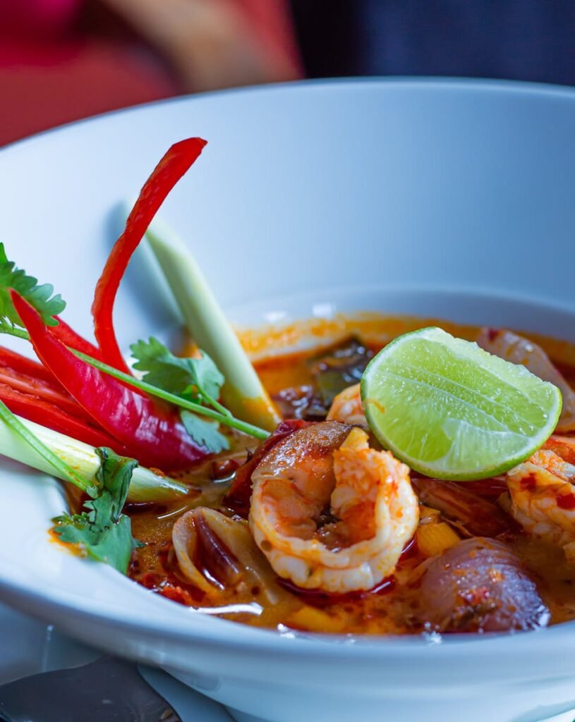Close-up of traditional Thai Tom Yum soup with shrimp and fresh herbs in a white bowl.