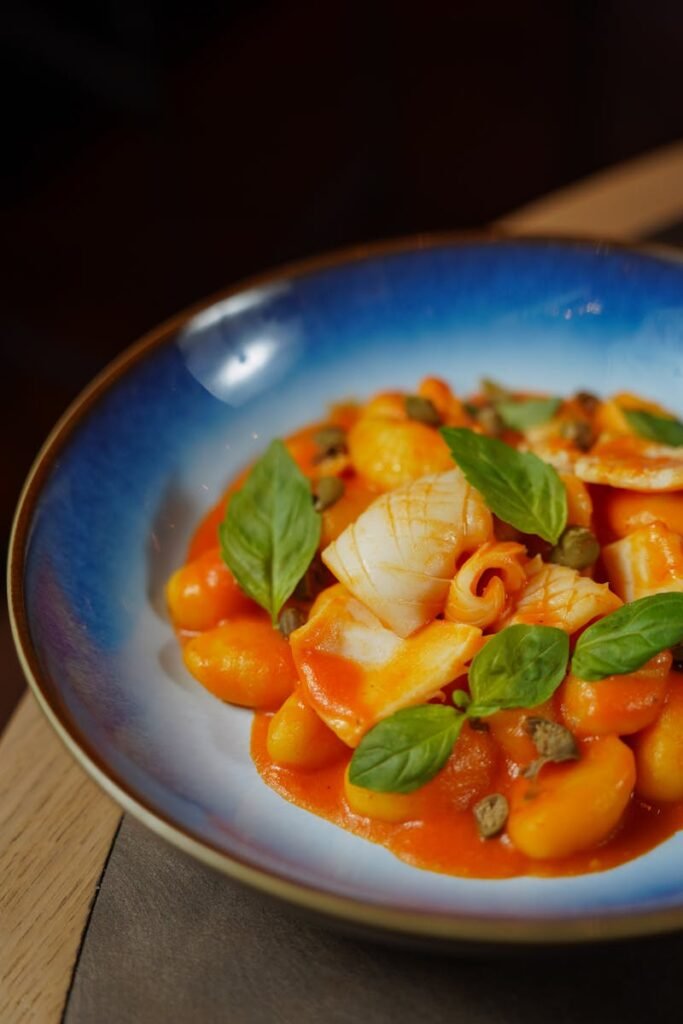 Close-up of pasta in red sauce garnished with basil leaves in ceramic bowl.