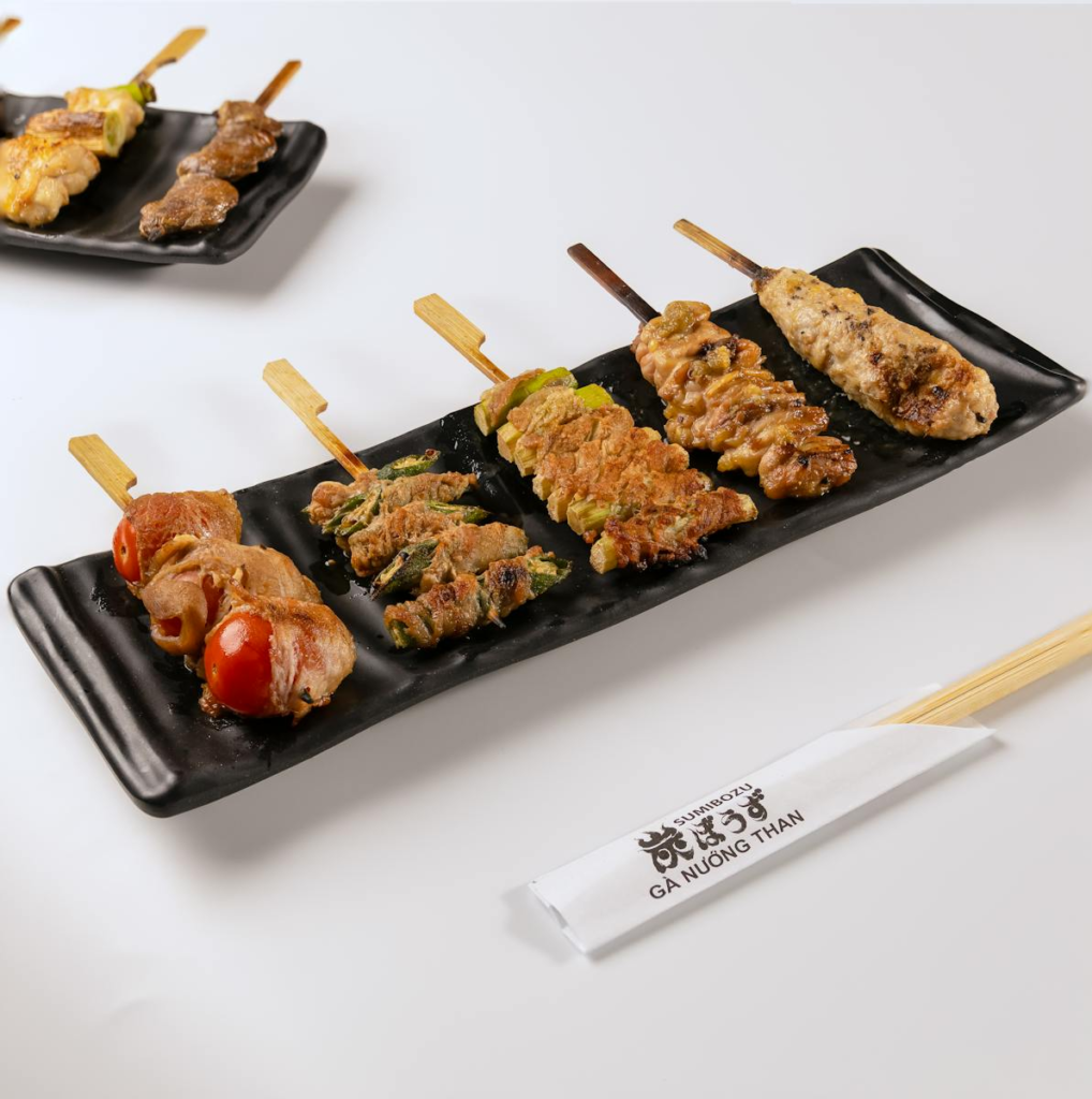 Assorted yakitori skewers served on elegant black plates with chopsticks.