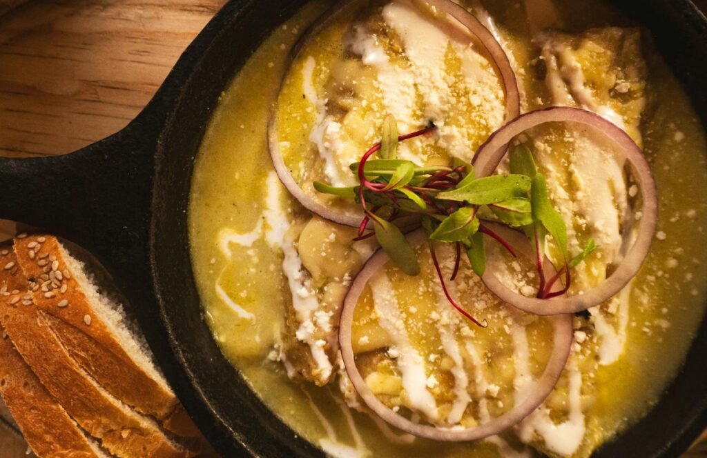 Close-up of Mexican Enchiladas Suizas garnished with red onion and cheese in a skillet.