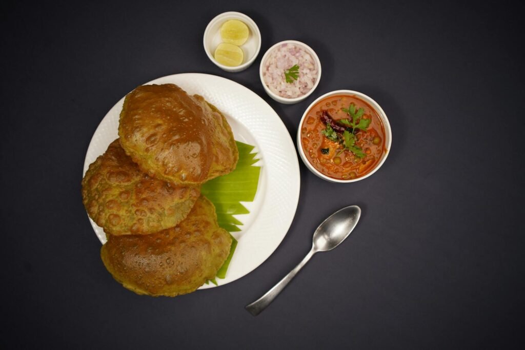 Top view of traditional Indian meal with poori, chana masala, and condiments on a white plate.