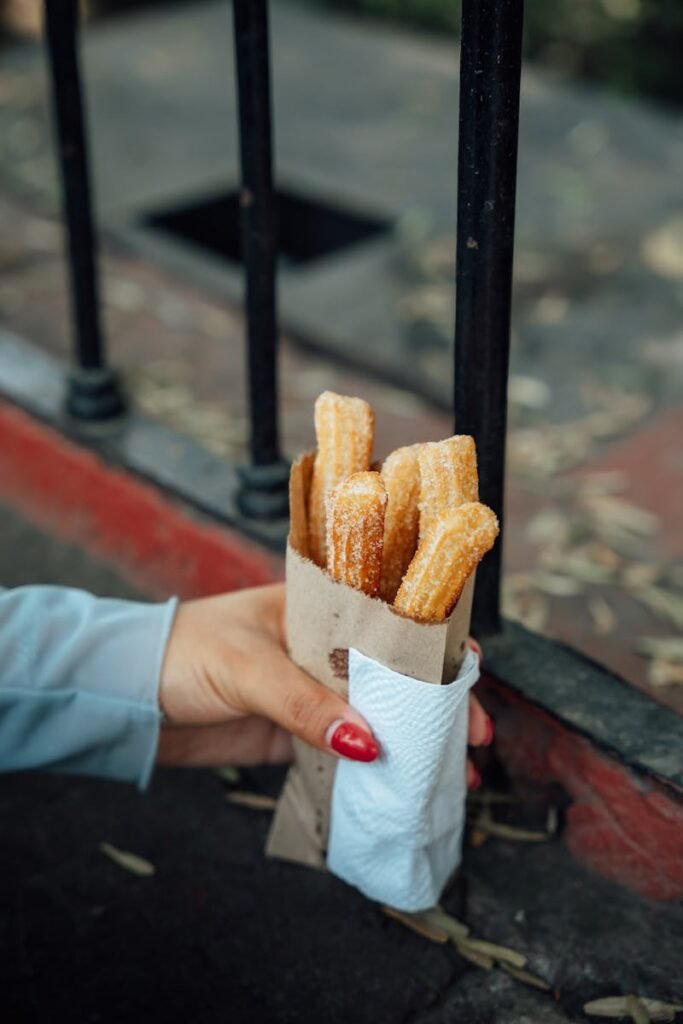 A hand holding sugar-coated churros wrapped in paper on a street in Ciudad de México.