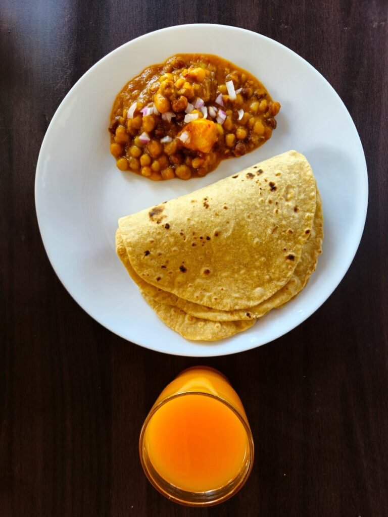 Overhead view of traditional Indian roti with chana masala and juice.