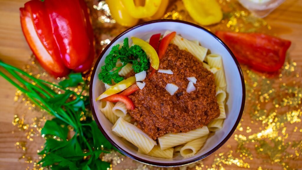 A bowl of pasta with Bolognese sauce garnished with bell peppers and parsley.