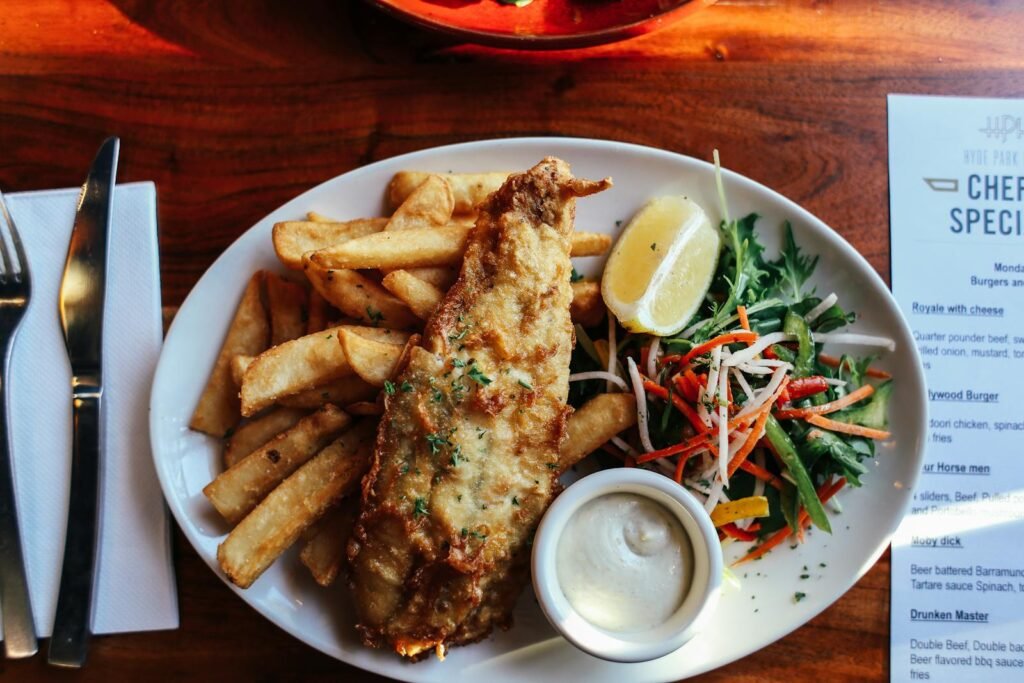 Top view of crispy fish and chips with fresh salad and tartar sauce on a wooden table.