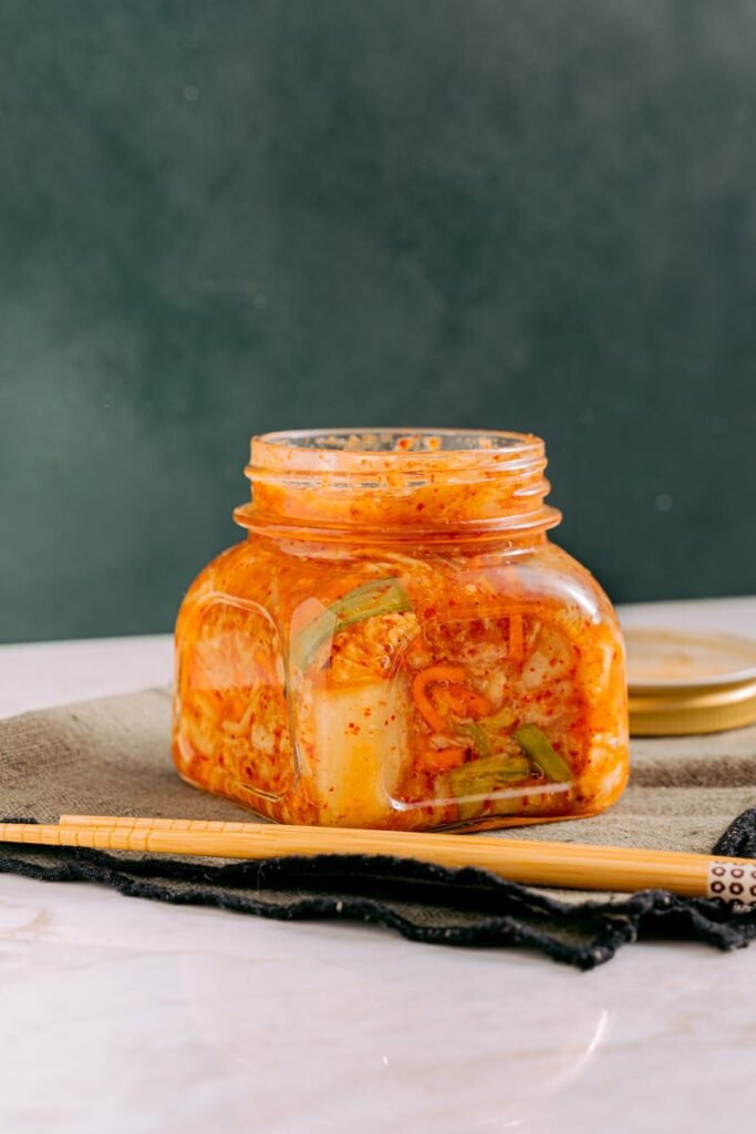 Close-up of homemade kimchi in a jar with chopsticks on a table.