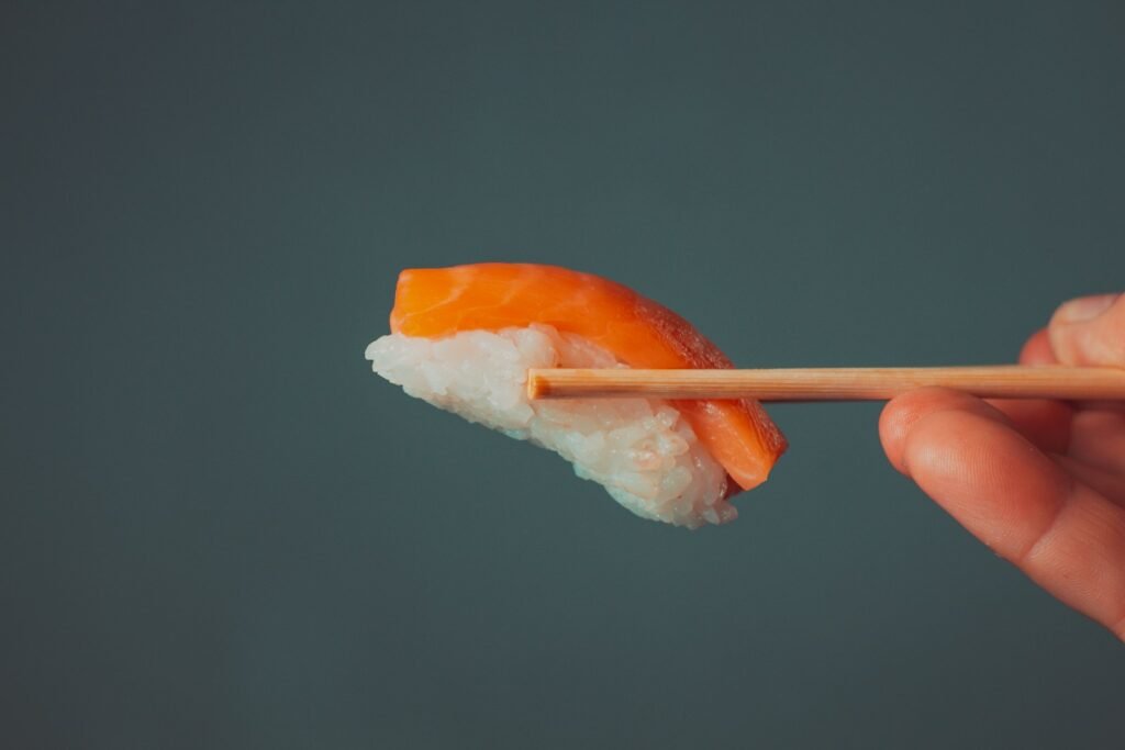 a hand holding a piece of sushi with chopsticks