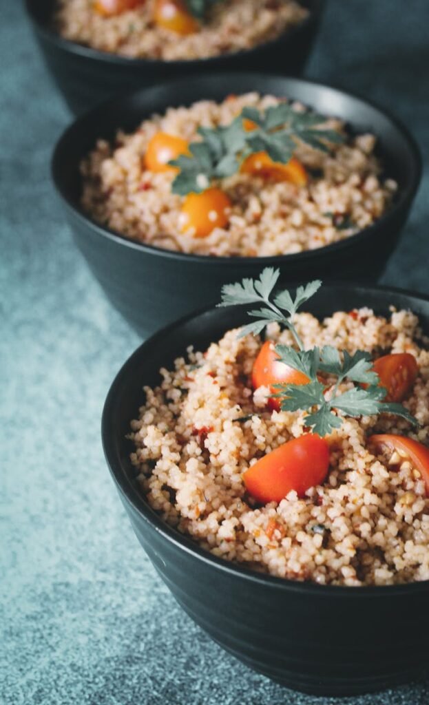 Close-up of delicious couscous with cherry tomatoes and parsley in black bowls.